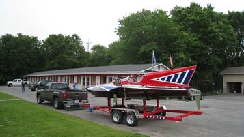 A trailer with a boat, parked in front of a building with a red and white facade.