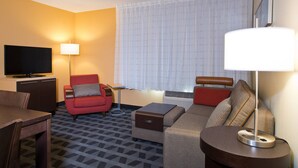 Una habitación de hotel con televisor, sillón rojo, sofá y lámpara.