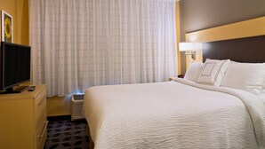 Una habitación de hotel con una cama grande, un televisor sobre un aparador de madera y una ventana con cortinas.