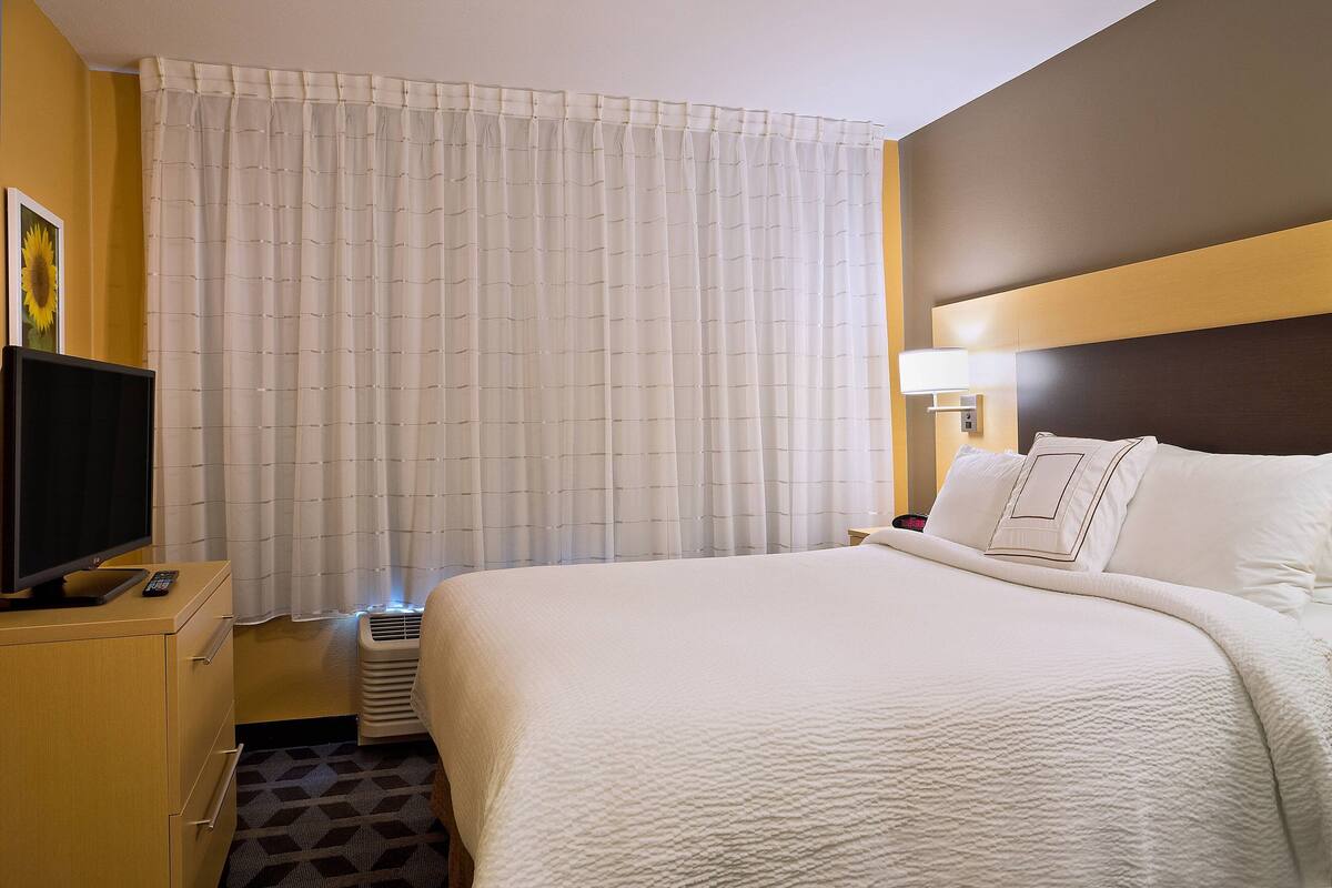 A hotel room with a large bed, a television on a wooden dresser, and a window with curtains.