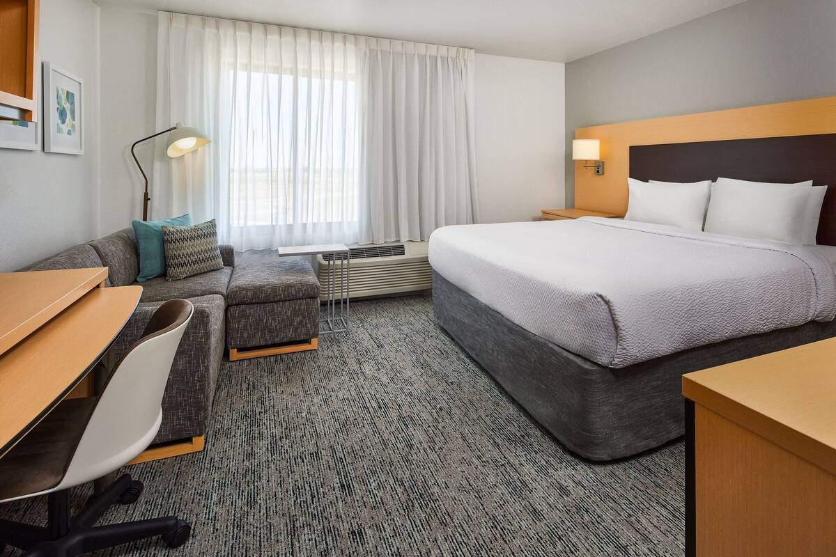 A hotel room with a bed, a desk, a chair, a sofa, and a standing lamp.