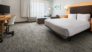 Una habitación de hotel con una cama, un escritorio con silla, un televisor, una lámpara y una ventana con cortinas.