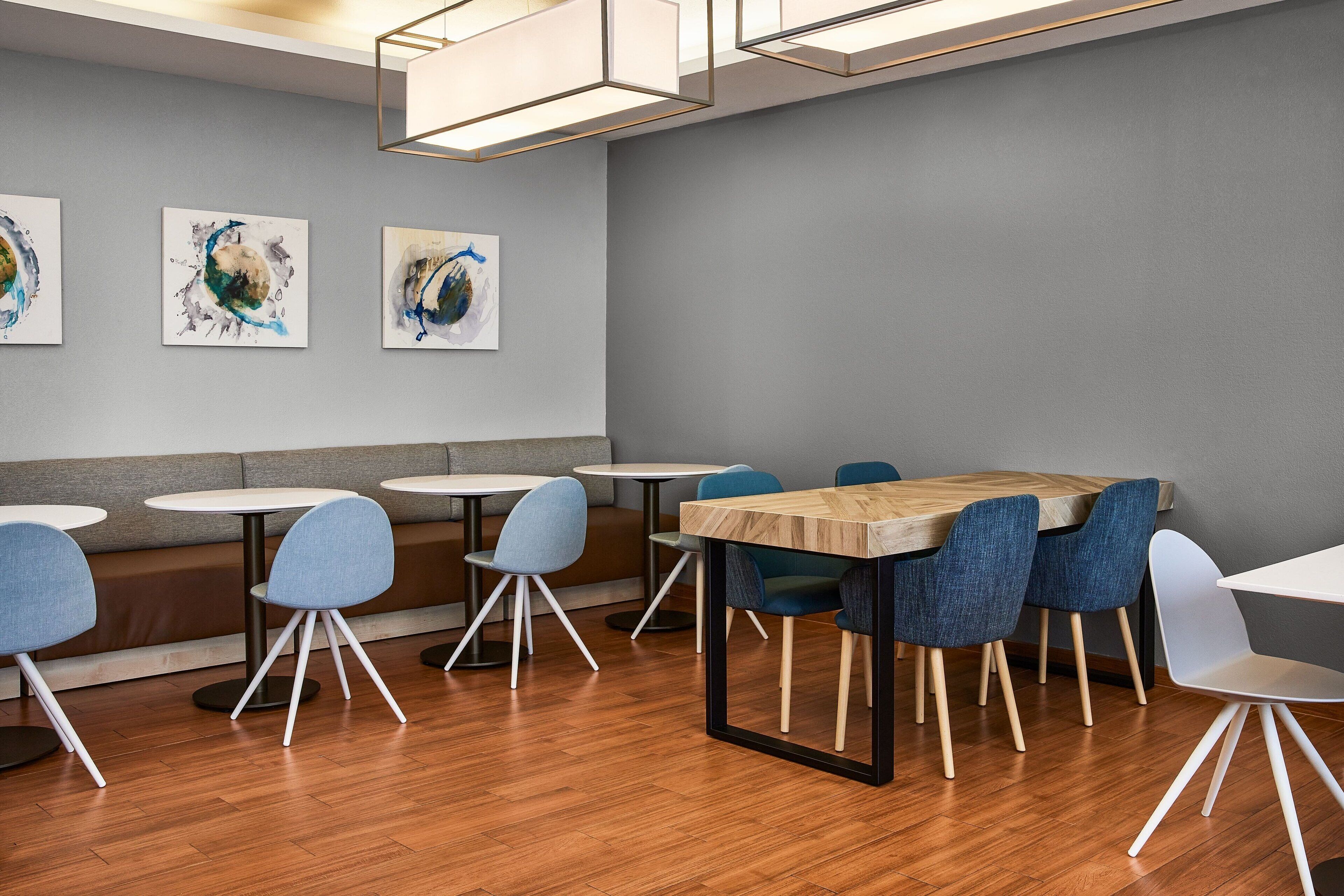A modern dining area with round tables, blue chairs, and abstract art on the wall.