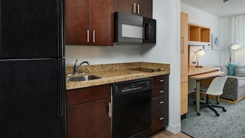 Una cocina compacta con armarios de madera oscura, un refrigerador negro, un microondas y un lavavajillas.