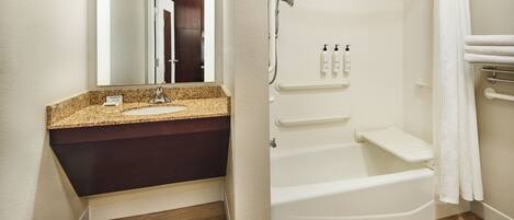 Une salle de bain avec un lavabo surmonté d’un plan en granit, une baignoire blanche et un espace douche.