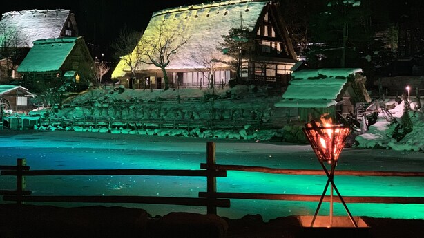En traditionell japansk by i nattens mörker, med snötäckta byggnader och en frusen flod.