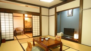 Ett traditionellt japanskt rum med tatamimattor på golvet, ett lågt träbord med teservis, en tv och en skjutdörr som leder till ett annat rum.