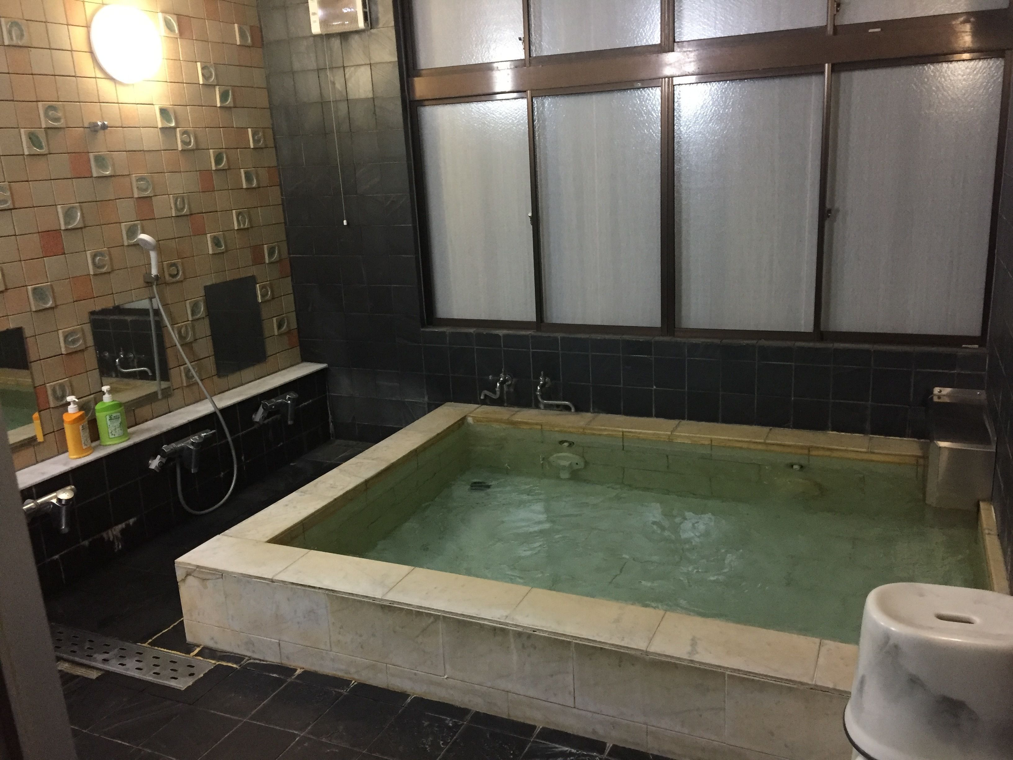 A bathroom with a large bathtub, a mirror, and a tiled wall.