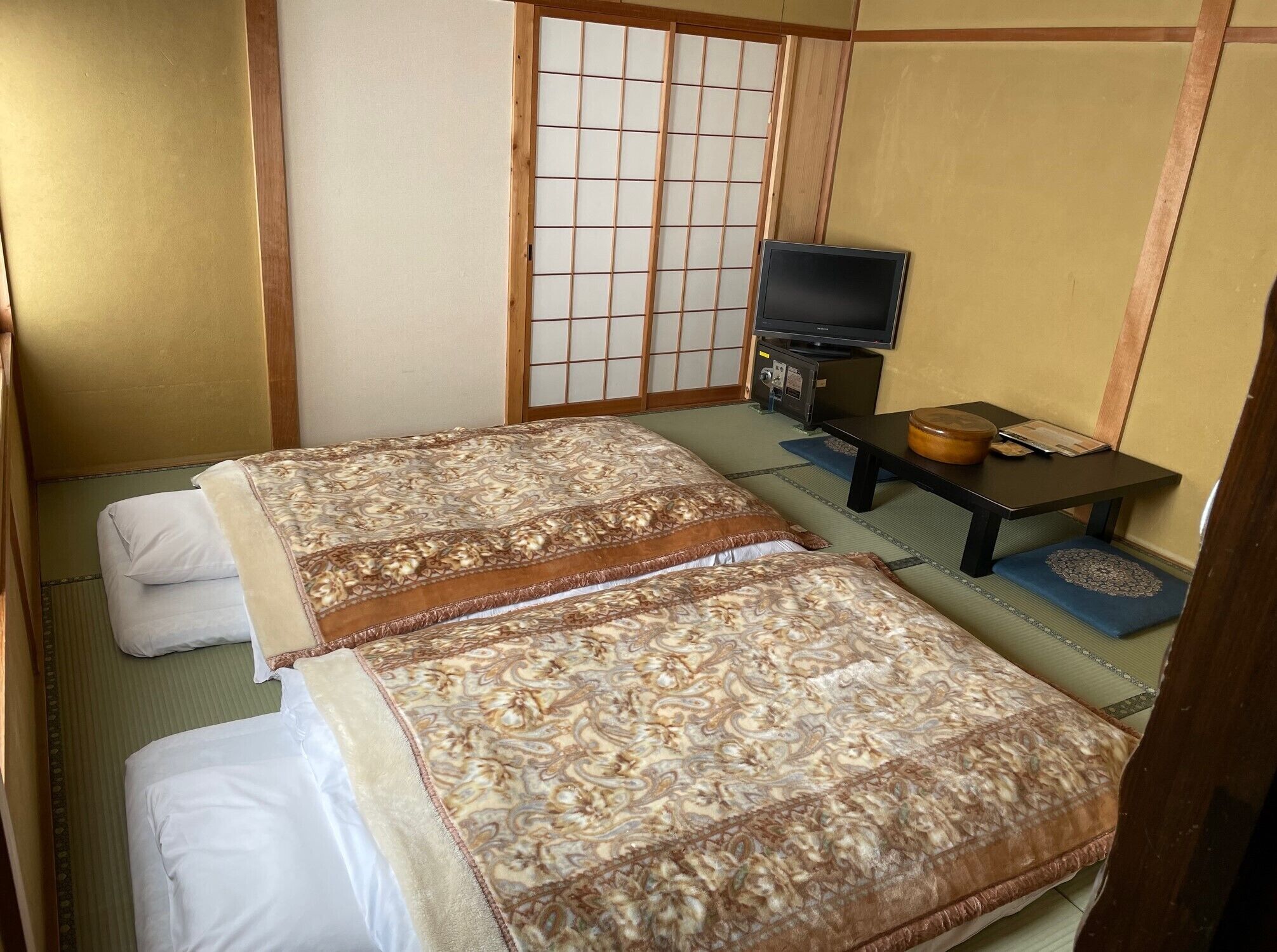 A traditional Japanese room with tatami flooring, a futon bed, a television, and a small table with a bowl and a book.