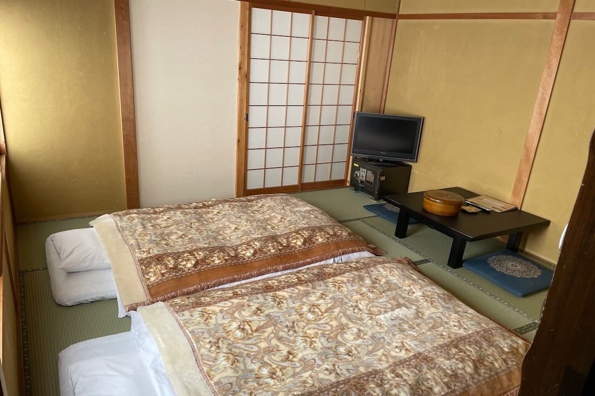 A traditional Japanese room with tatami flooring, a futon bed, a television, and a small table with a bowl and a book.