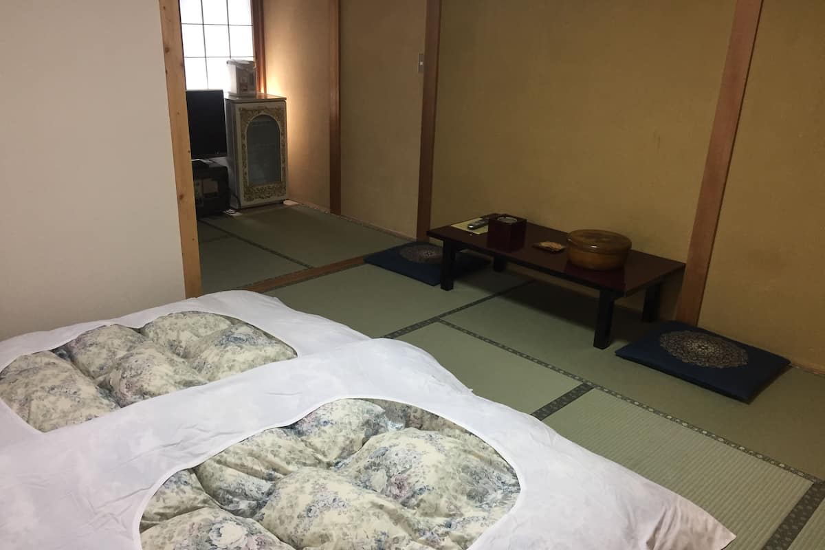 A traditional Japanese room with tatami flooring, a low table with a tea set, and a bed with floral bedding.