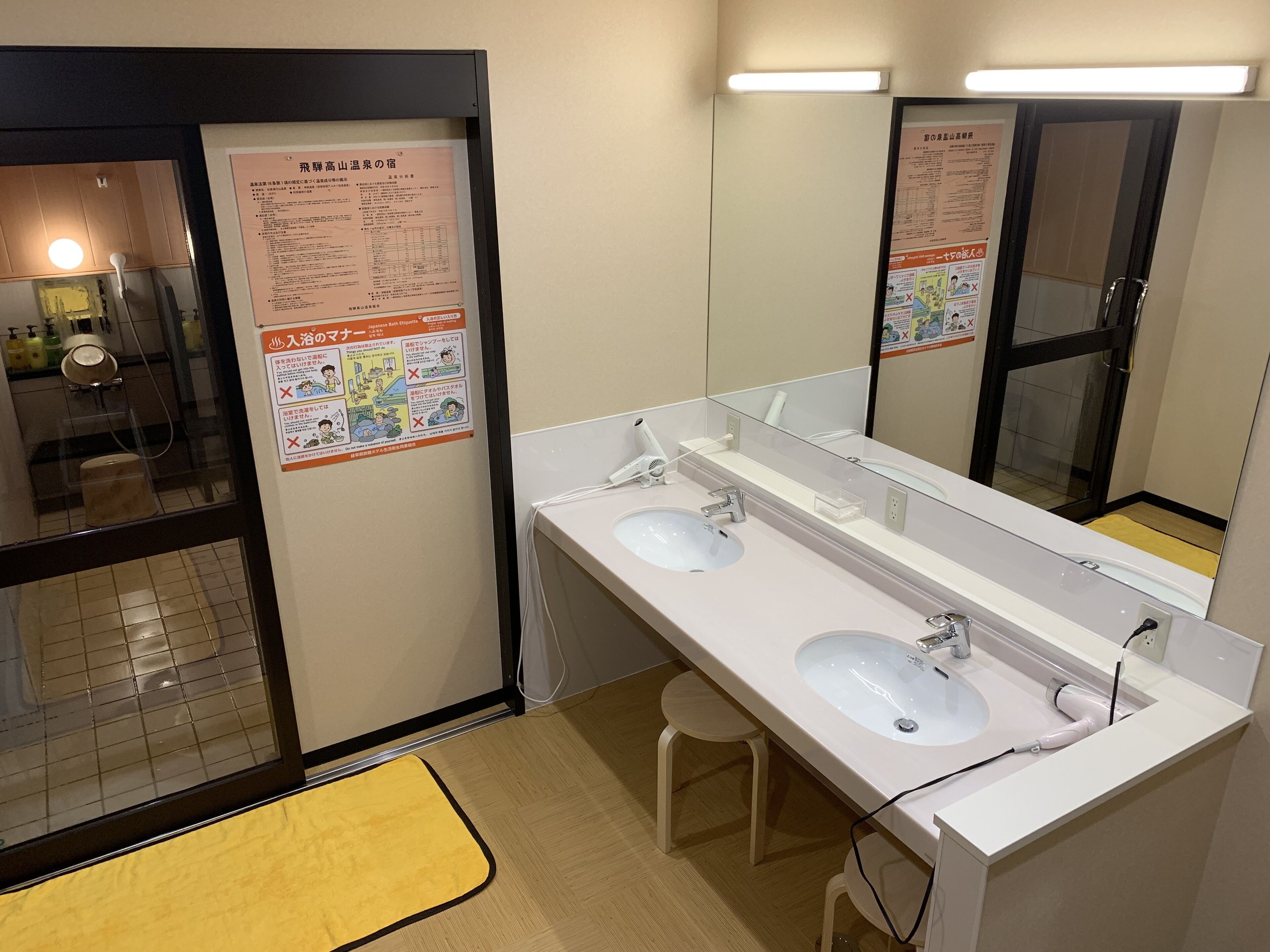 A hotel bathroom with two sinks, a mirror, and a yellow mat.