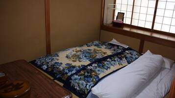 A small, neatly arranged room with a bed, a wooden table, and a window with a view.