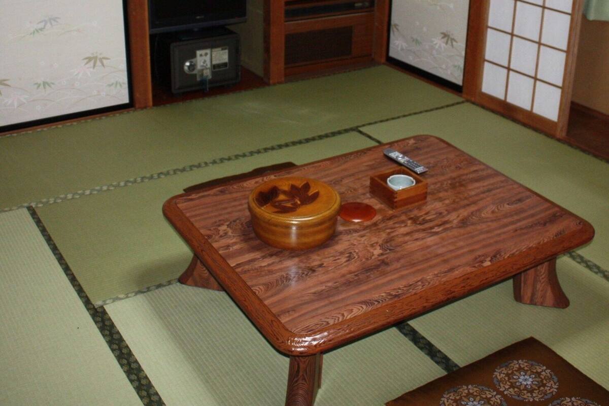 A traditional Japanese room with tatami flooring, a low wooden table with a bowl and a remote control, and sliding doors with floral patterns.