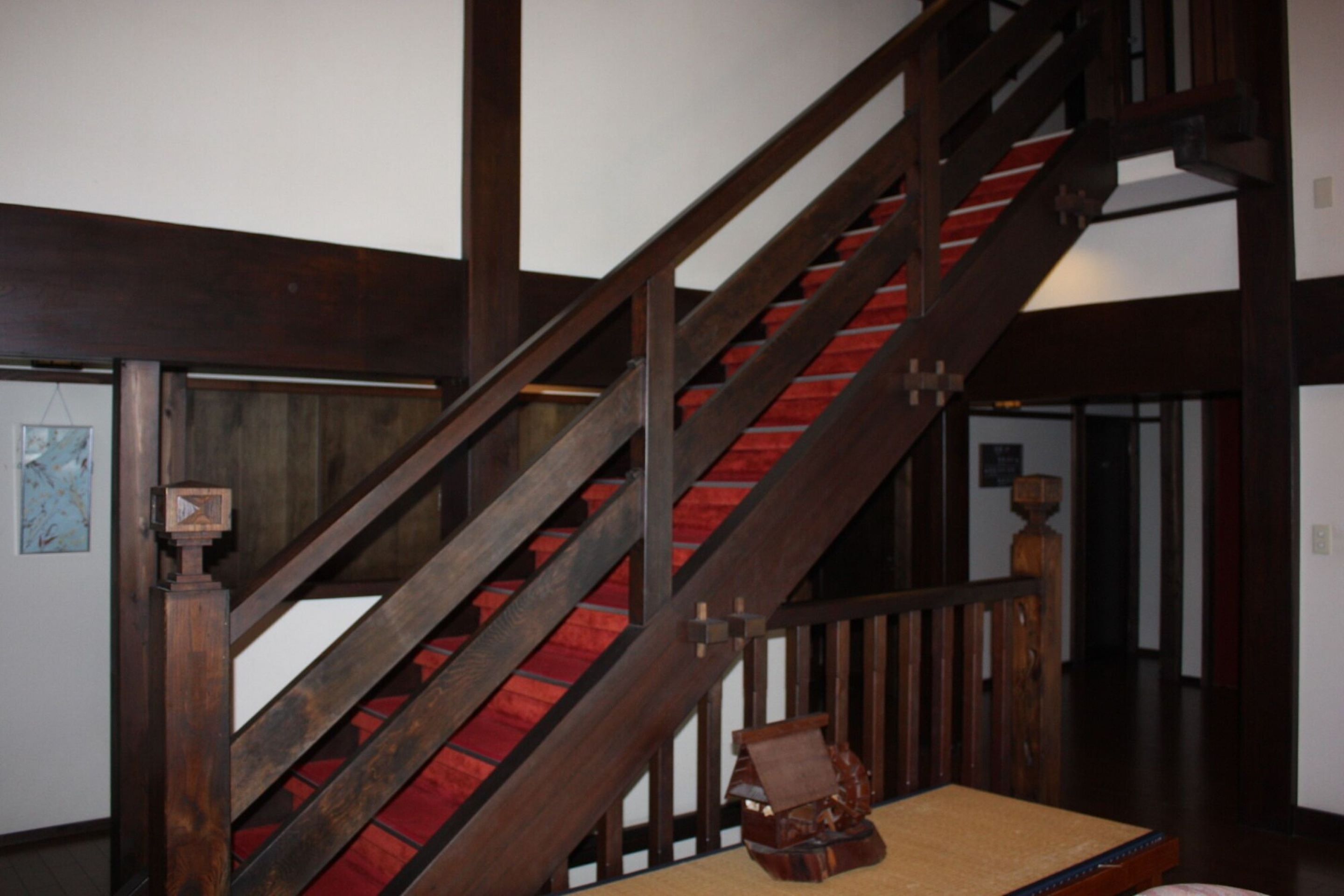 Un escalier en bois avec des marches recouvertes d’une moquette rouge et une main courante en bois.