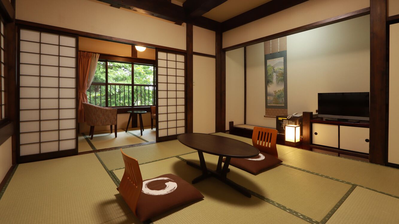 A traditional Japanese room with tatami flooring, a low table, chairs, a television, and a sliding door leading to a balcony.