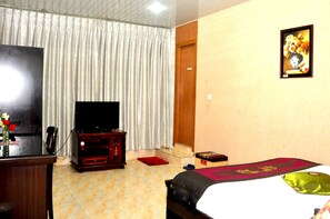 Ein Hotelzimmer mit einem Bett, einem Fernseher, einem Holzschrank, einem roten Teppich und einem Bild an der Wand.