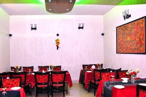 Un comedor con mesas dispuestas para cuatro comensales, cada una con mantel rojo y sillas a juego.