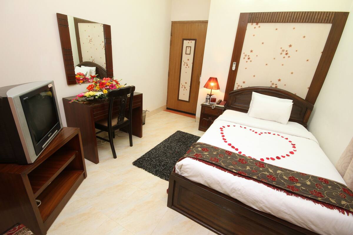 A hotel room with a bed, a desk with a TV, a mirror, and a door with a decorative panel.
