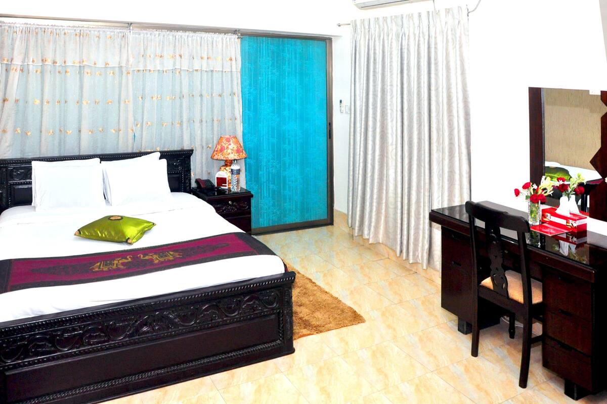 A hotel room with a large bed, a desk, a chair, and a mirror.