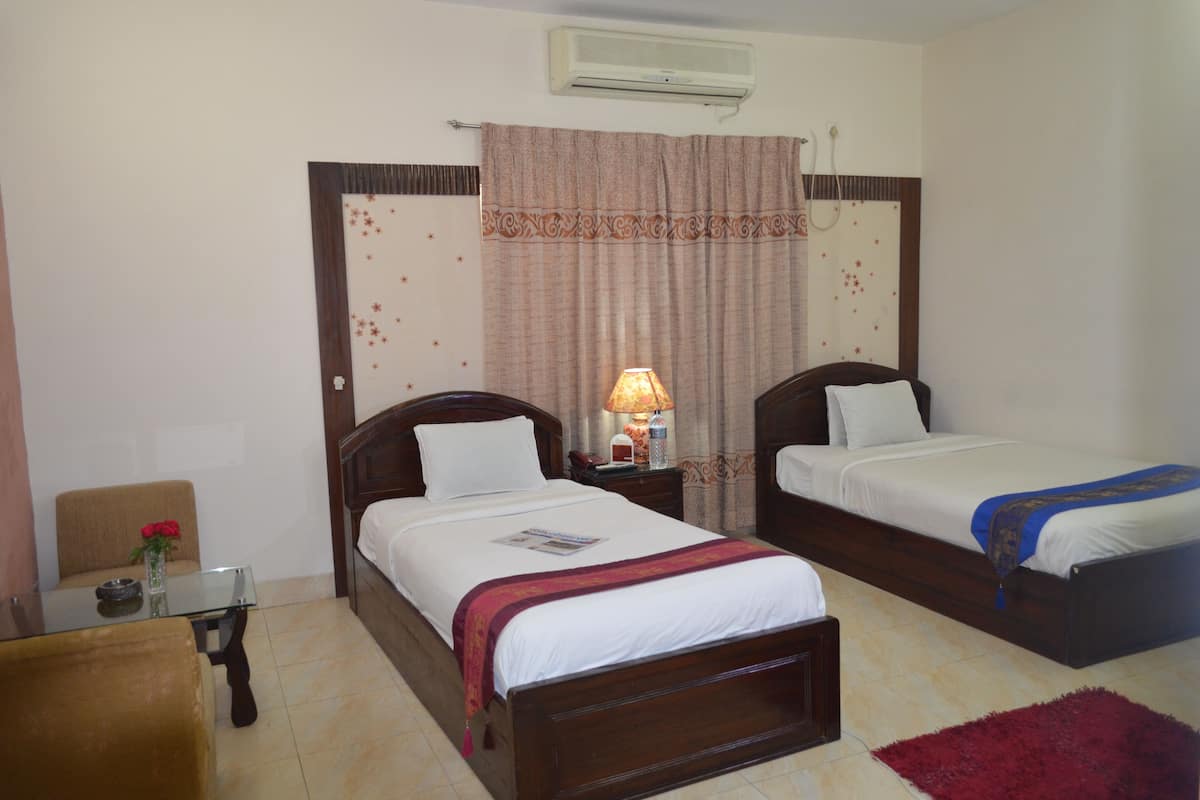 A hotel room with two single beds, a small table with a vase of flowers, a chair, and a red rug.