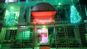 A hotel entrance with a neon sign, a red carpet, and green Christmas lights. - Hotel Rose Garden (Dhaka)