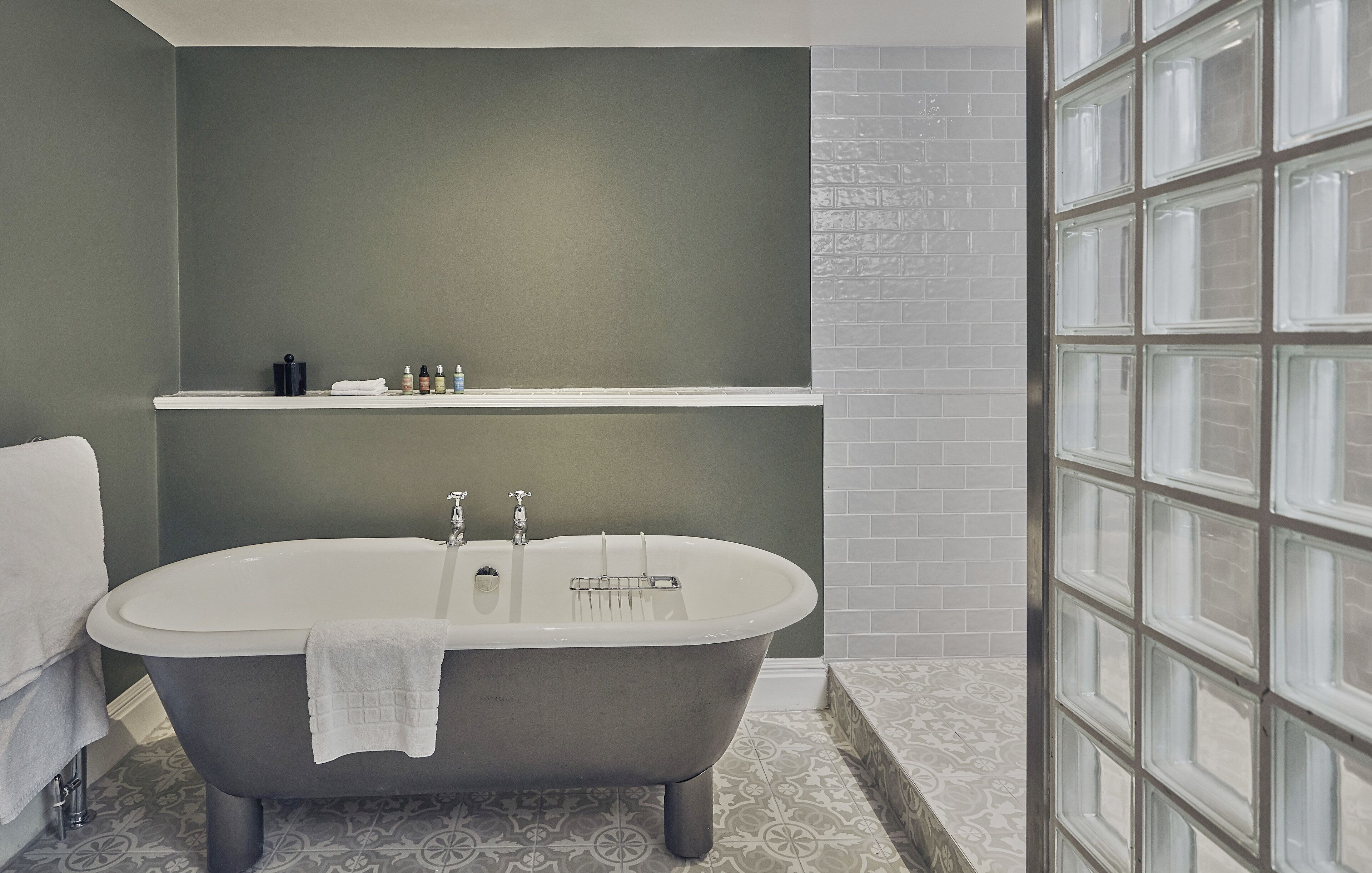 A bathroom with a freestanding bathtub, a shelf with toiletries, and a patterned floor.