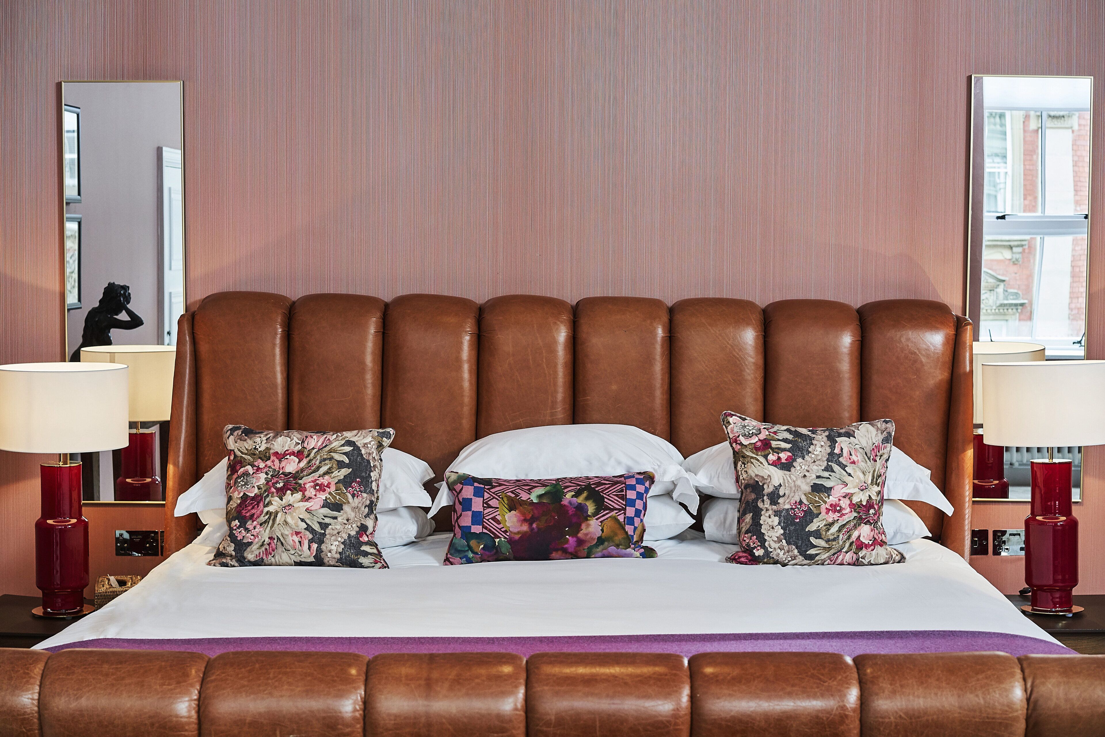 Een opgemaakt bed met hoofdeinde, twee bedlampen en kussens met bloemenprint.