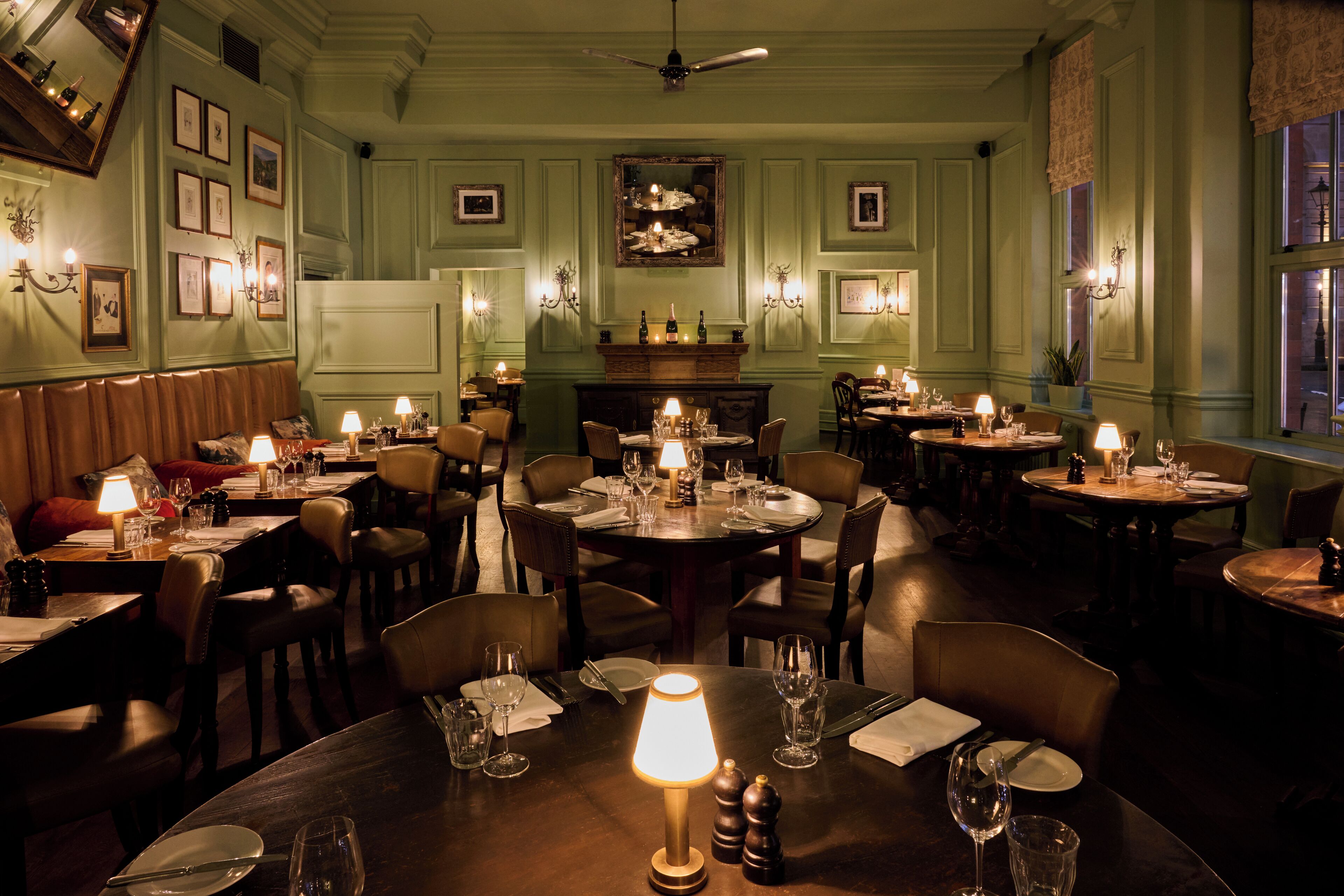 Un espace repas avec plusieurs tables dressées pour le dîner, chacune agrémentée de bougies et d’une belle décoration.