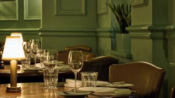 A dining table set with plates, glasses, and a wine glass, with a lamp on the left.
