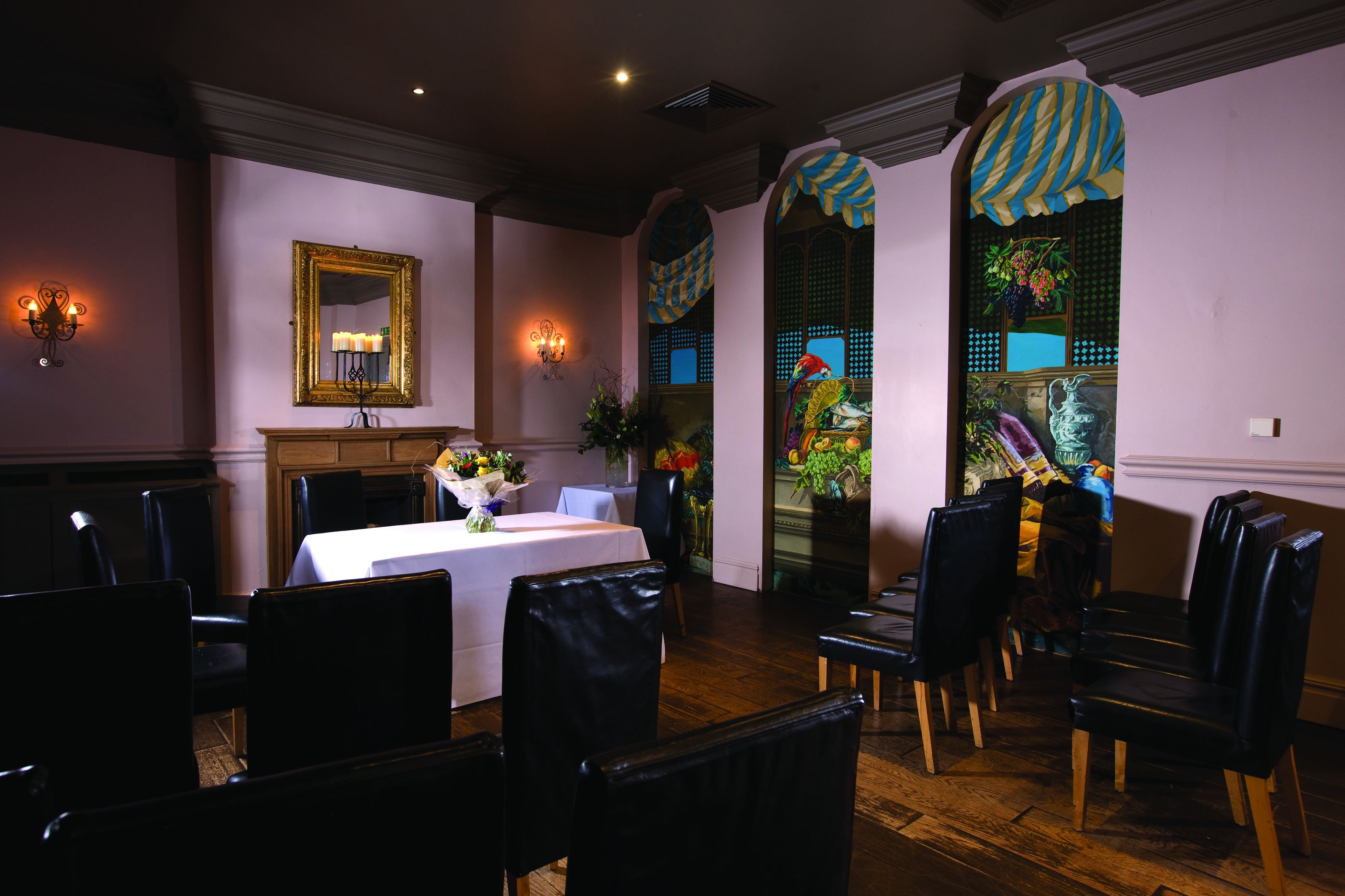 A dining area with a table set for four, black upholstered chairs, a white tablecloth, and a mirror on the wall.