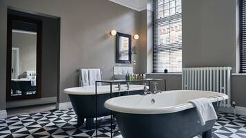 A bathroom with two freestanding tubs, a large mirror, and a window with blinds.