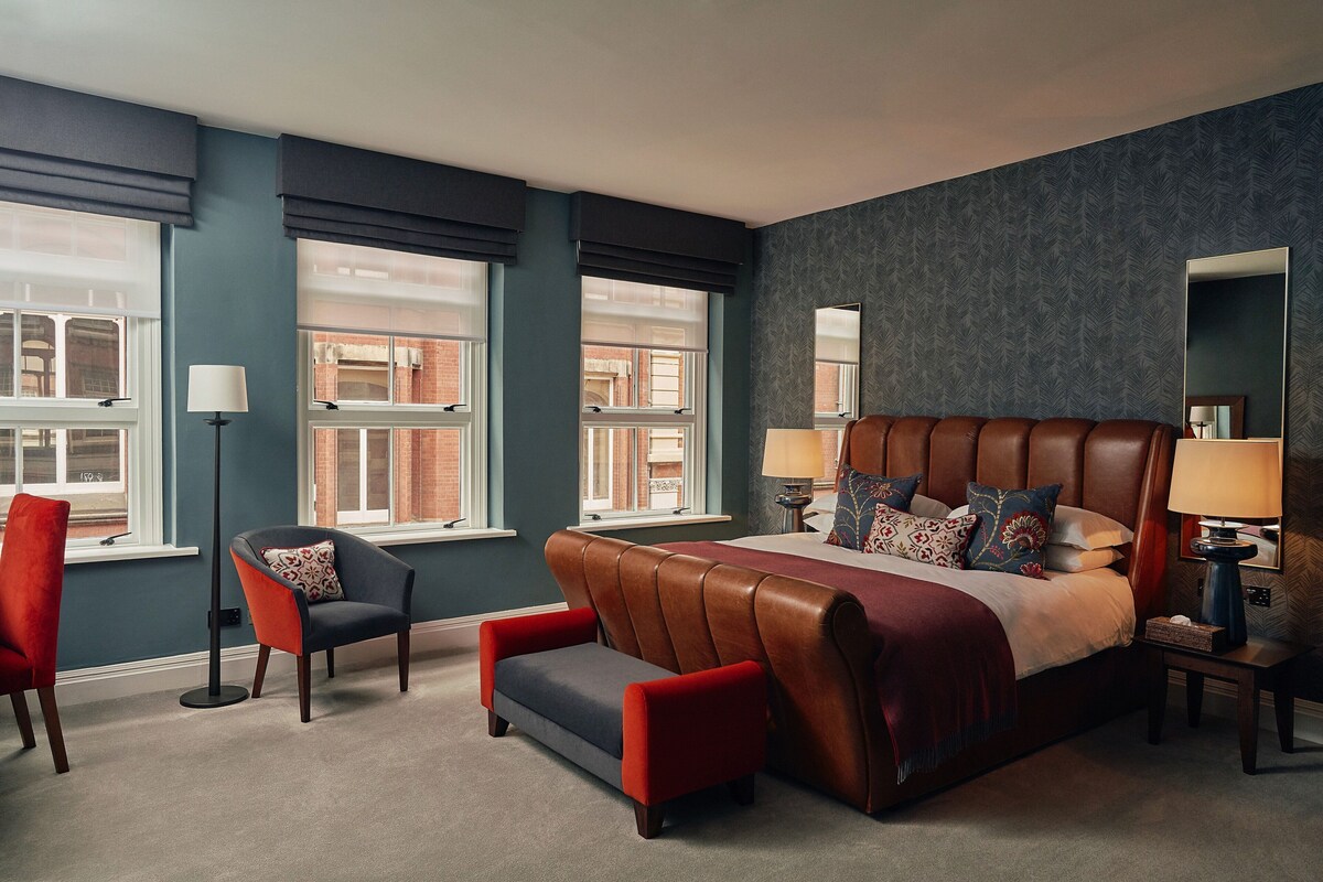 A bedroom with a large bed, a red armchair, a black armchair, and a floor lamp.