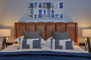 Una cama bien hecha con un cabecero marrón, dos lámparas de noche y un cuadro abstracto azul en la pared.