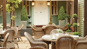 Eine Terrasse im Freien mit Korbmöbeln, Glastischen und Lichterketten.