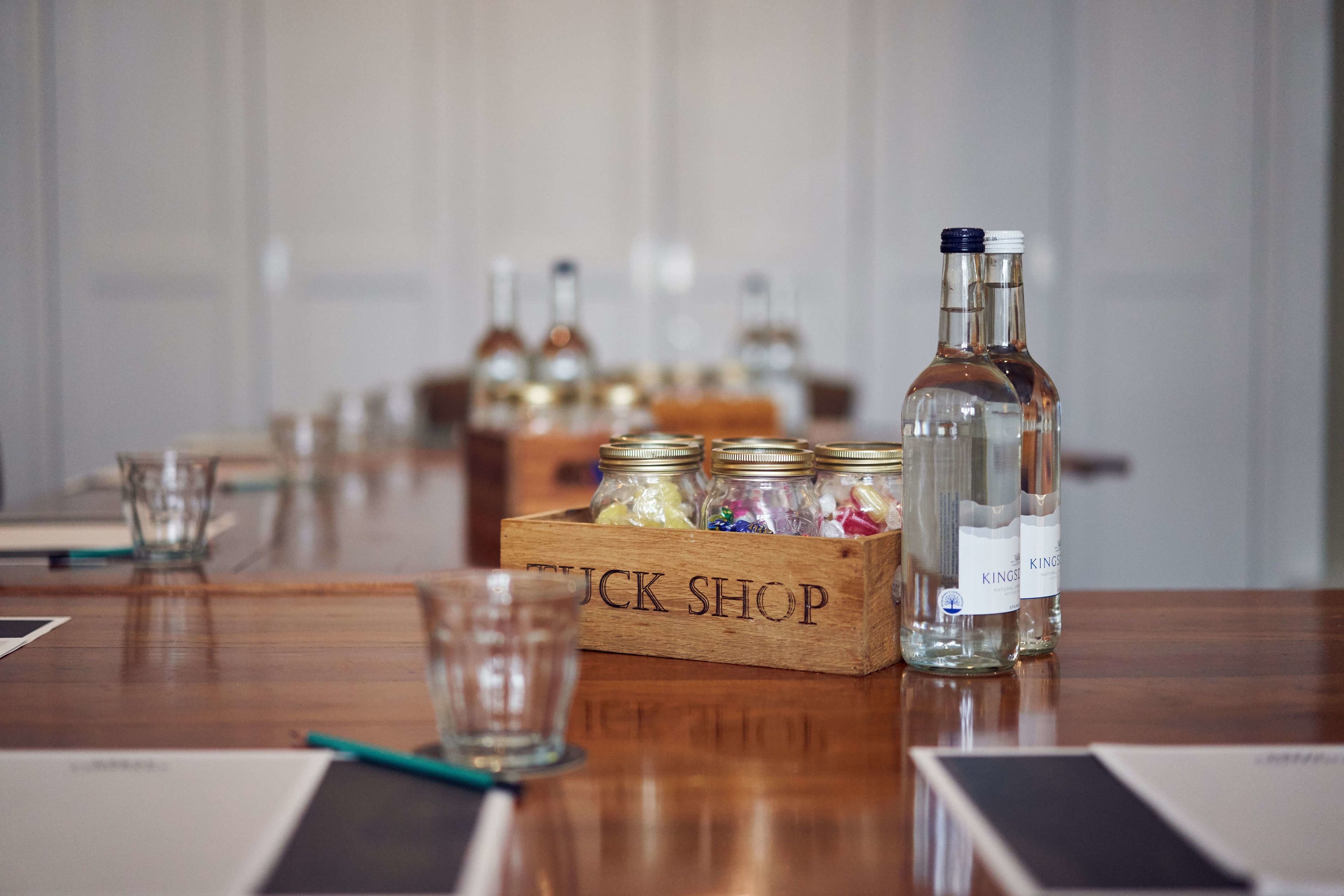 A wooden table with a box labeled "TUCK SHOP" containing colorful items and two bottles labeled "KING'S".