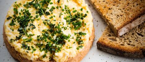 A round dish of scrambled eggs topped with chopped green onions, accompanied by slices of whole grain bread.