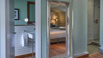 A bathroom with a white tiled wall, a large mirror, and a wooden floor.