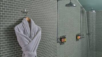 Une salle de bain avec un mur en briques grises, une serviette suspendue, une douche avec un pommeau de douche à main et un panneau de commande mural avec des flacons.