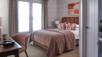 A hotel room with a bed, a desk, a chair, a lamp, and a window with curtains.