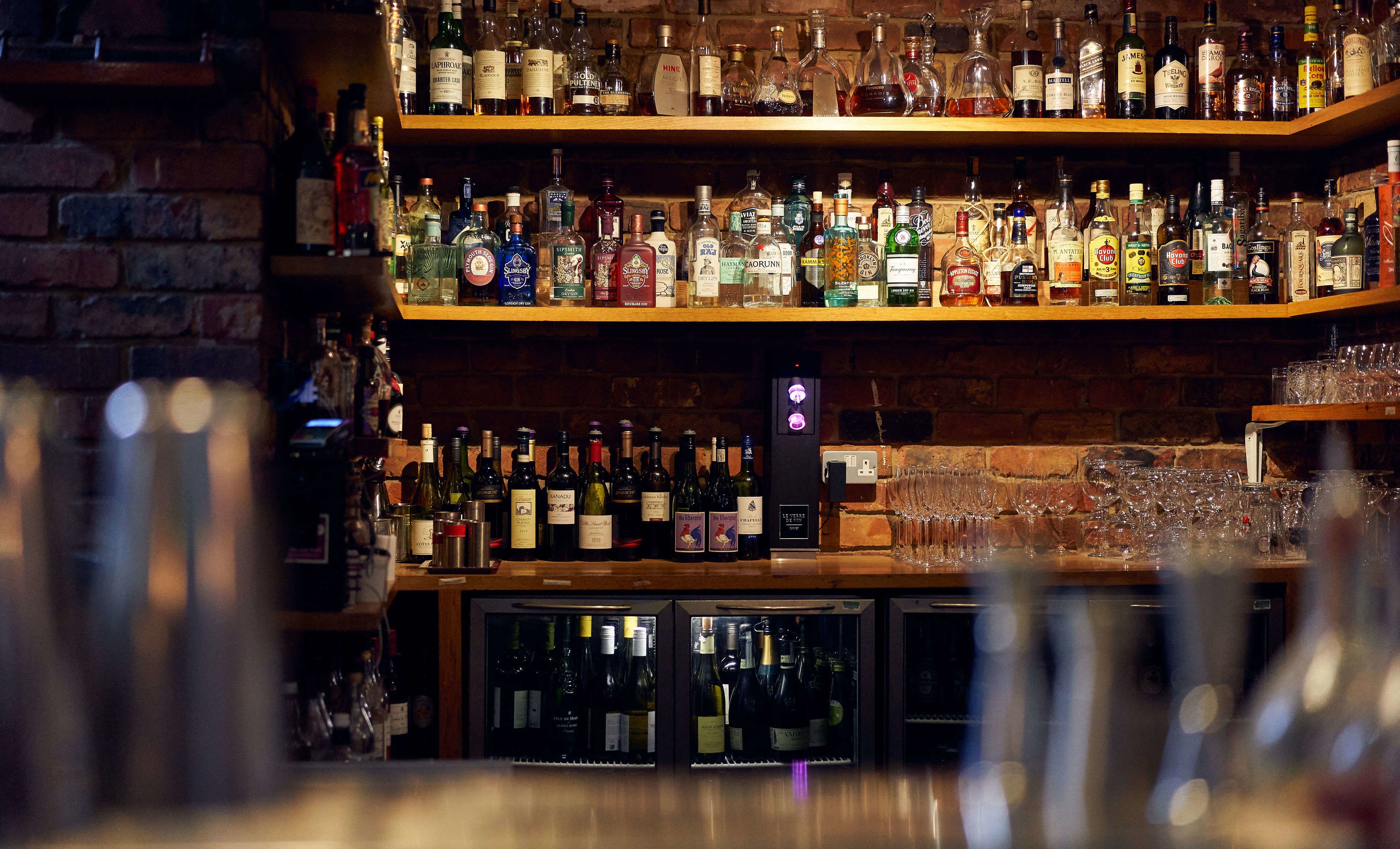 Een barruimte met planken vol verschillende drankflessen en glazen.