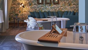 Ein Badezimmer mit einer freistehenden Badewanne, einem Waschtisch mit Spiegel und einer Couch im Hintergrund.