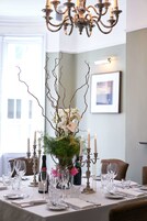 A dining table set for a meal with candles, a bottle of wine, and a vase of flowers.