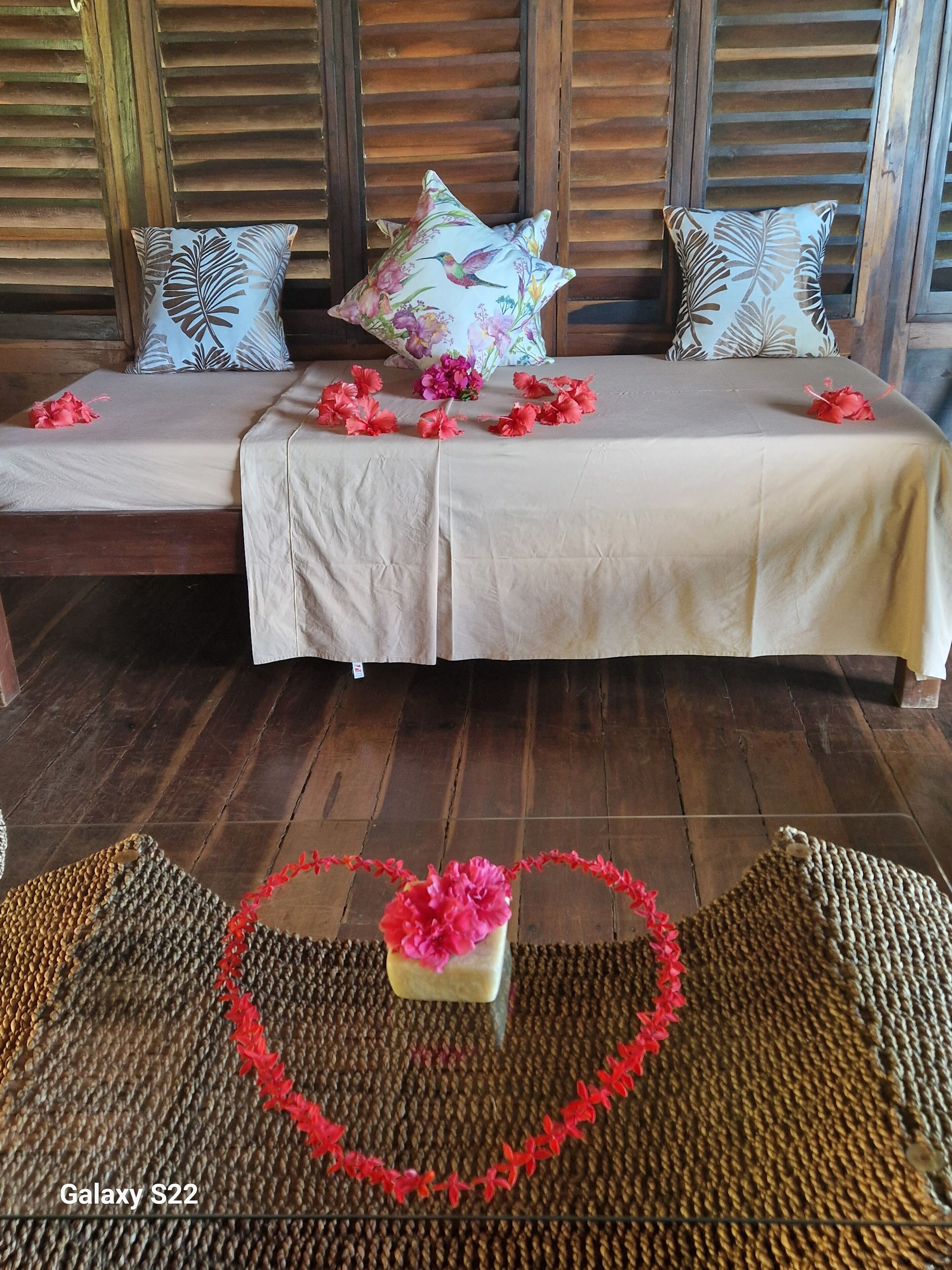 A bed with floral pillows, a heart-shaped decoration on the floor, and a woven rug.