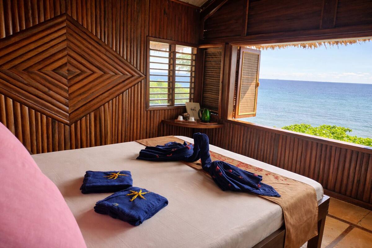 A wooden room with a bed, towels, and a view of the ocean.