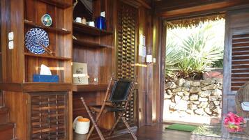 A wooden interior with a wooden floor, a chair, a table with a vase, and a view of the outside.