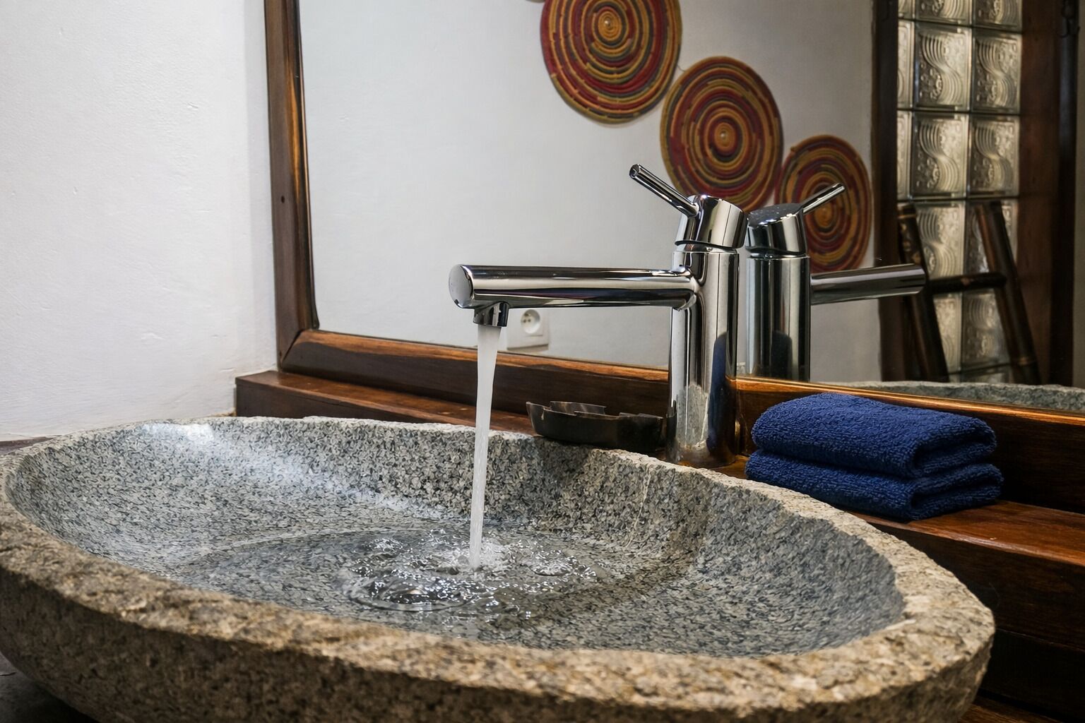Un lavamanos de piedra con agua corriente, una toalla azul y un espejo que refleja un adornado muro.