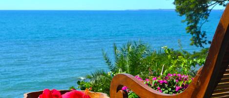 A wooden bench with a woven seat and a bowl of red flowers on a wooden table by the sea.