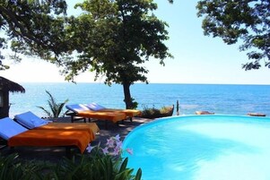 Zona junto a la piscina con sillones de descanso y una vista despejada del mar.