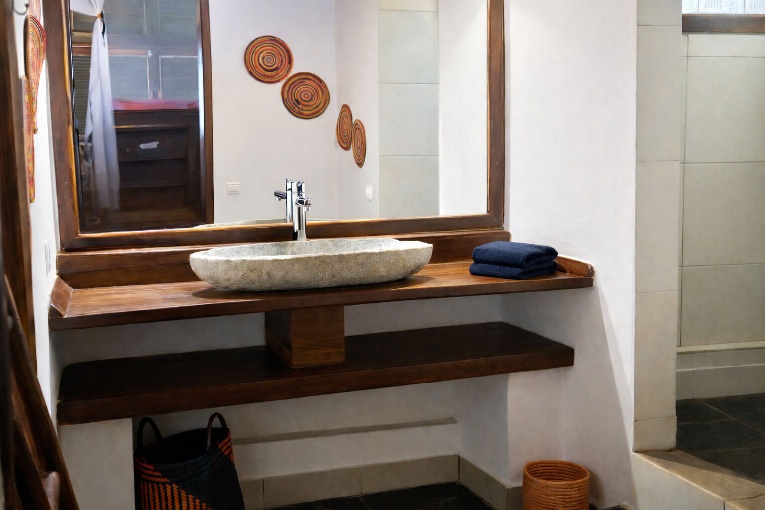 A bathroom with a stone sink, wooden shelves, a mirror, and decorative wall art.